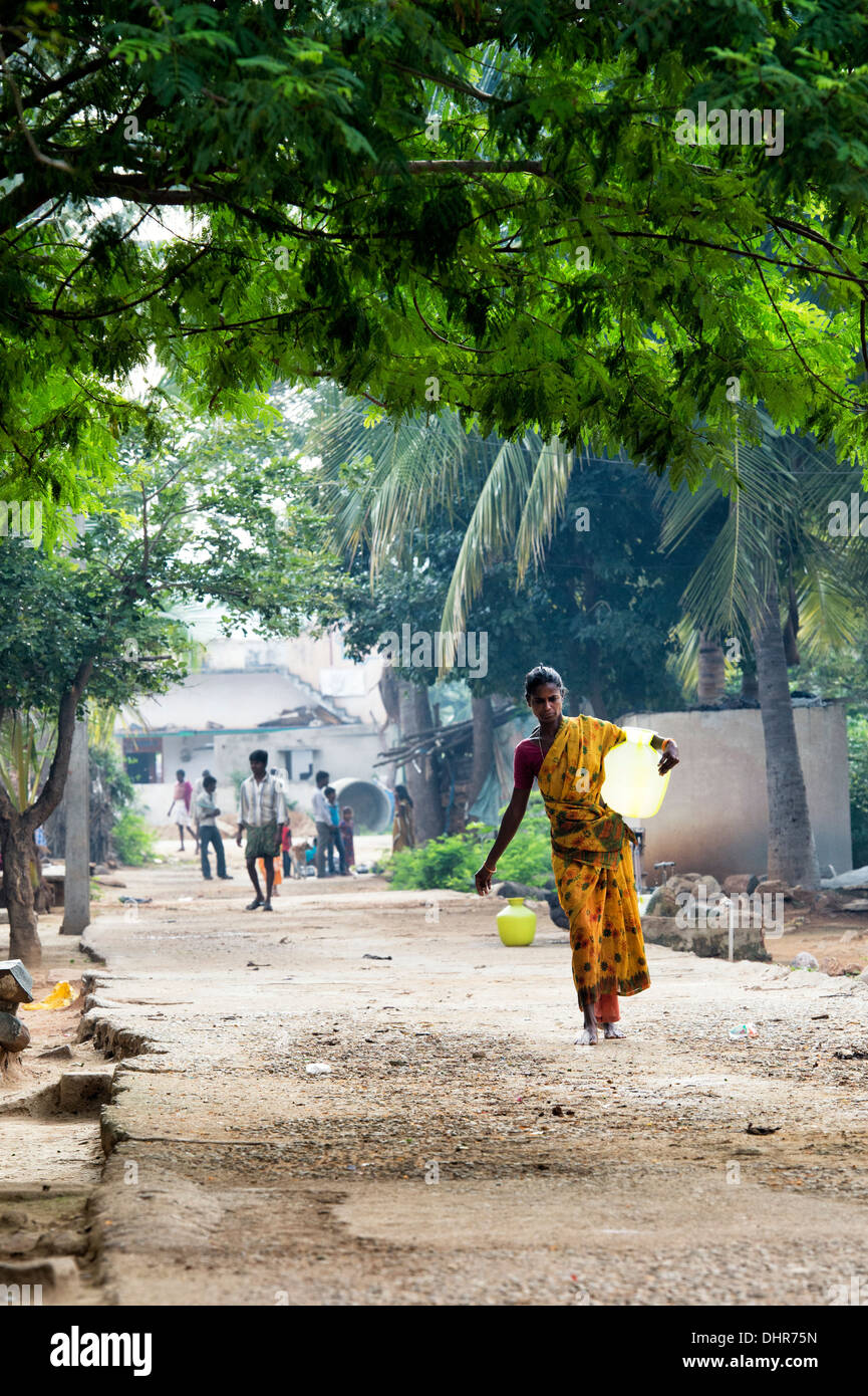 Indian woman carrying a plastic pot with water from a standpipe in a rural Indian village street. Andhra Pradesh, India Stock Photo