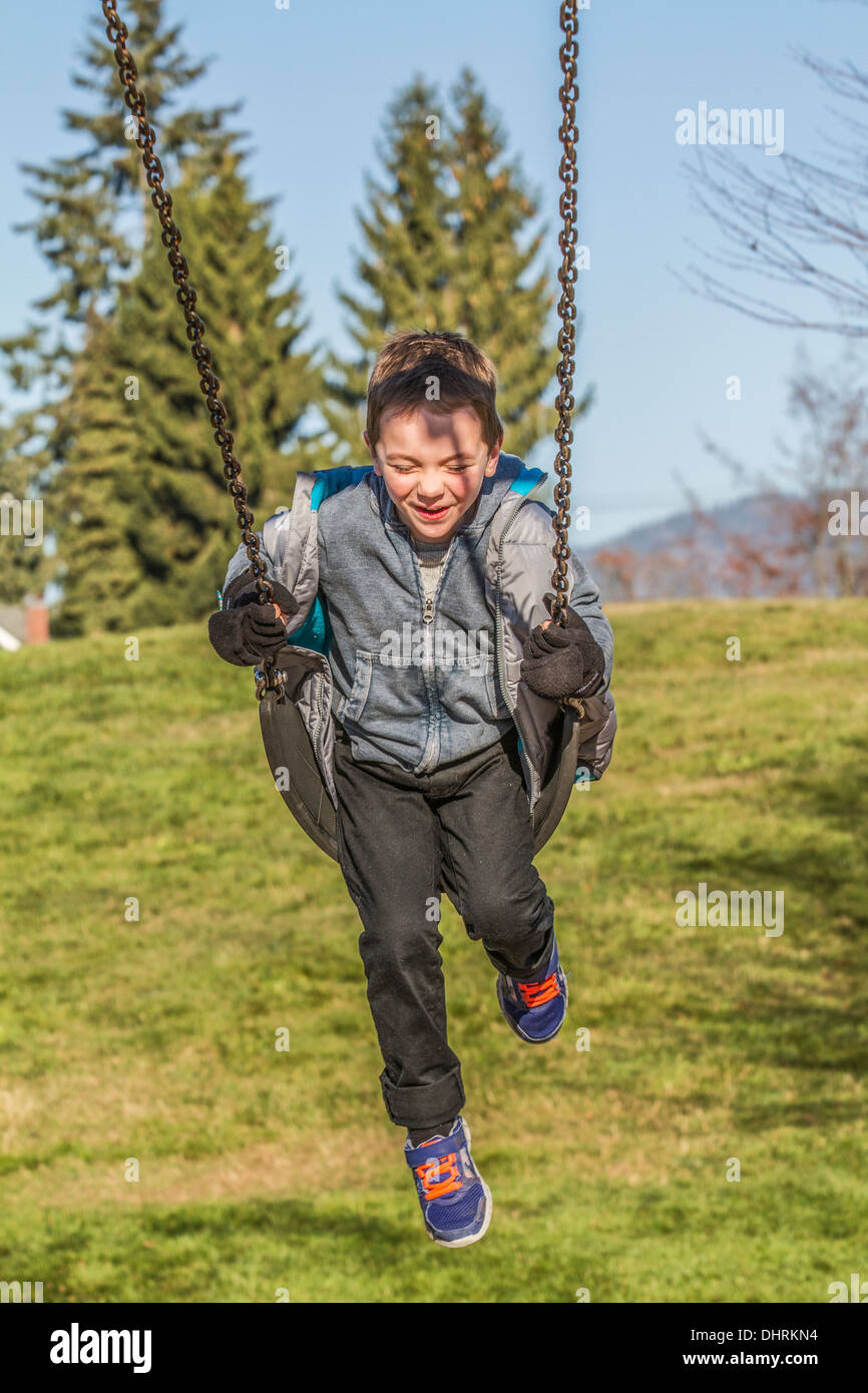 Model released, cute, smiling, laughing, 5 year old boy, having fun in the outdoors on playground swing. Stock Photo