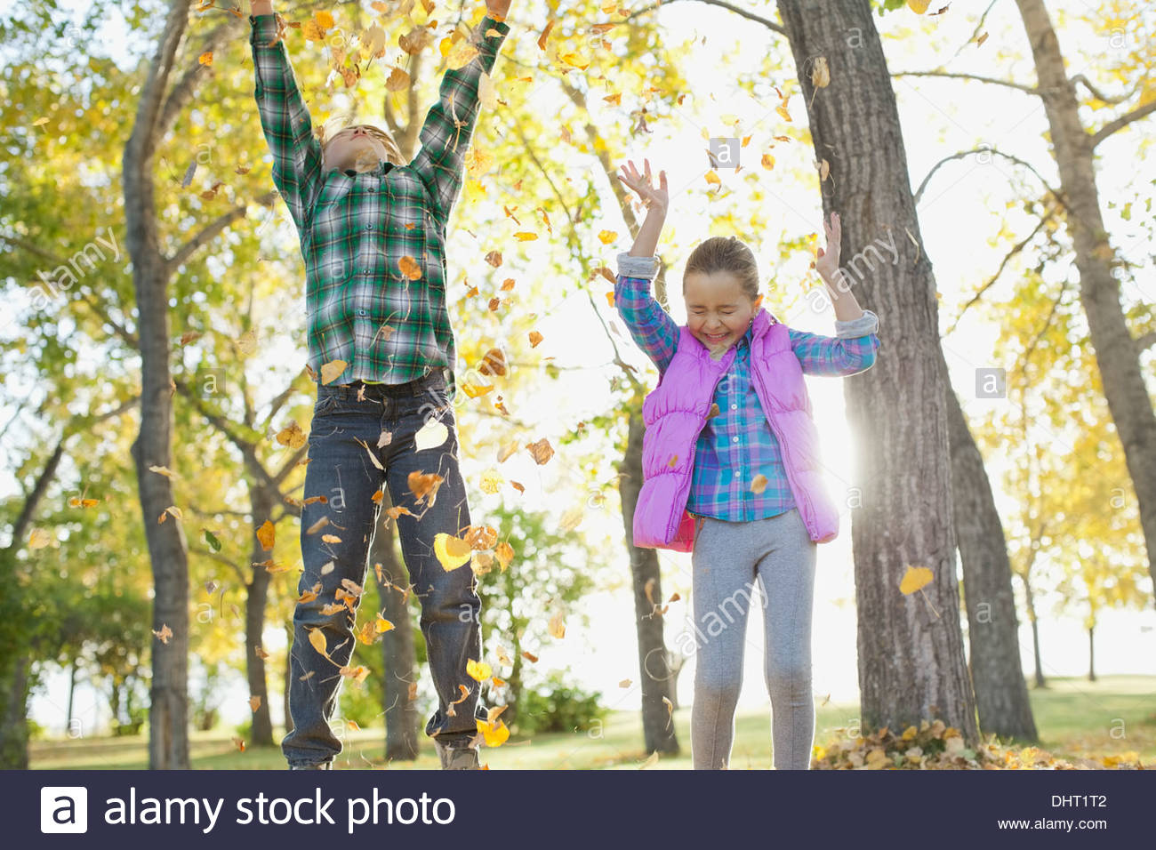 Cheerful siblings playing with leaves in park during autumn Stock Photo