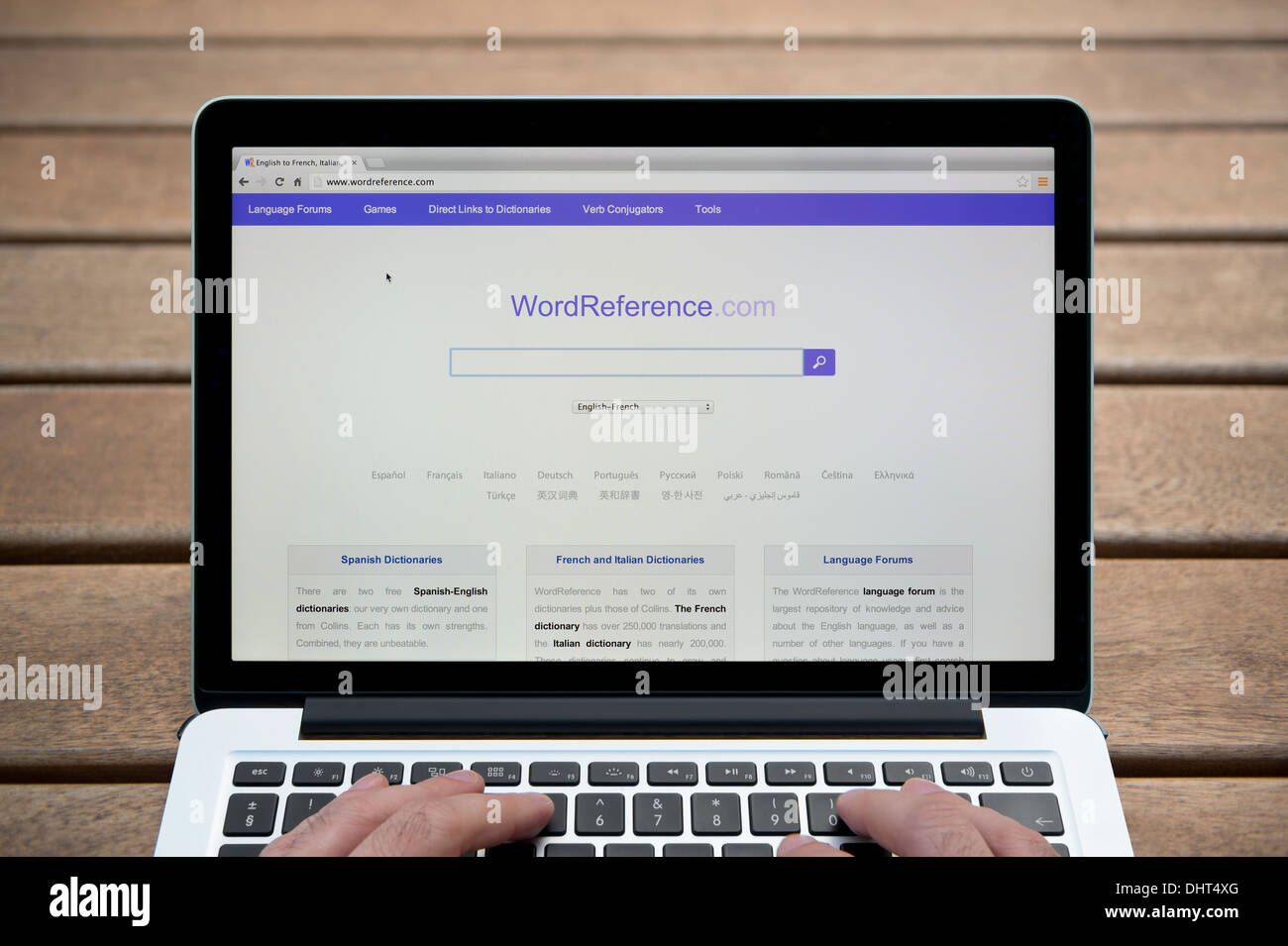 The Word Reference website on a MacBook against a wooden bench outdoor background including a man's fingers (Editorial use only) Stock Photo