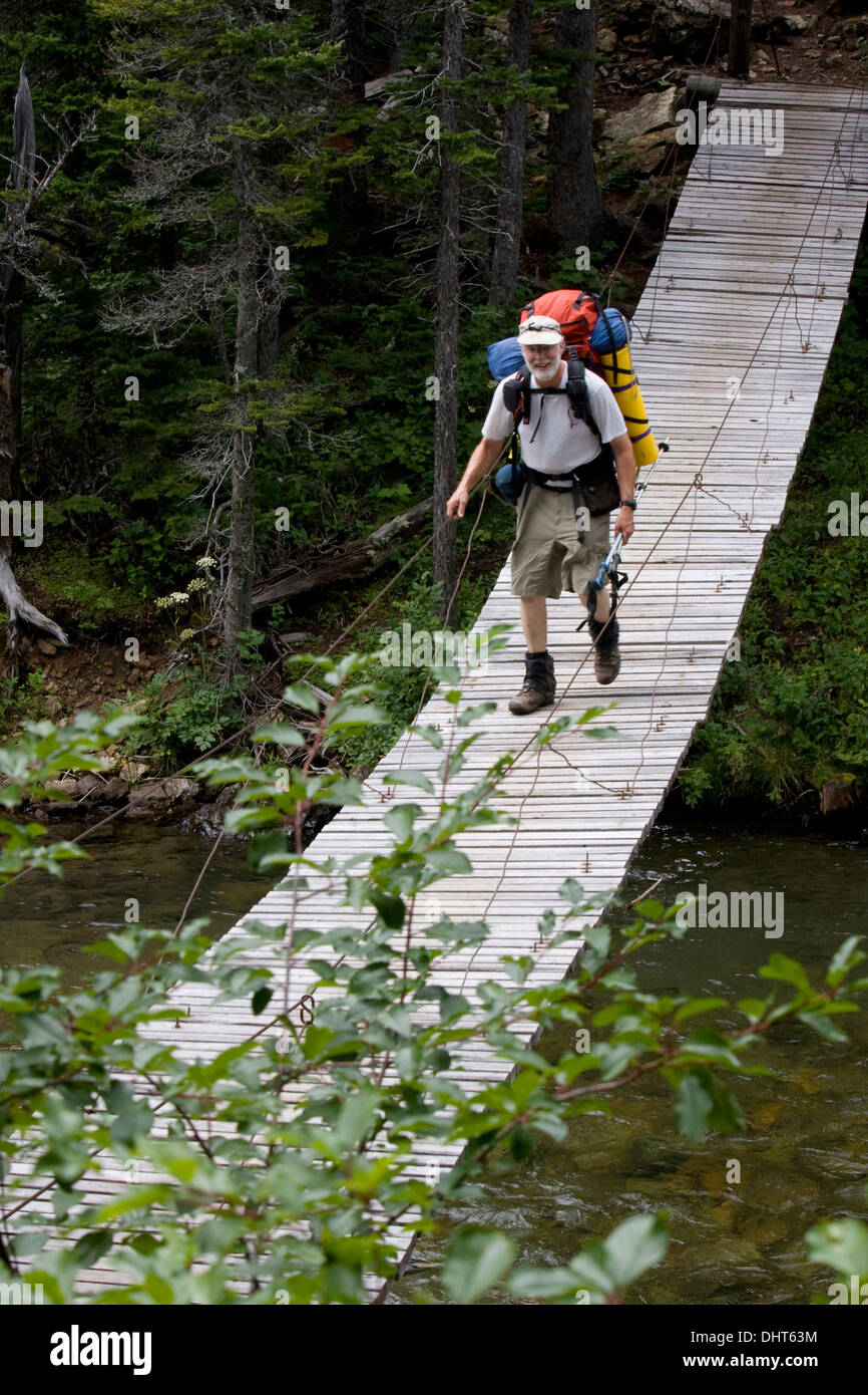 A hiker crosses the Belly River on a suspension bridge, Glacier