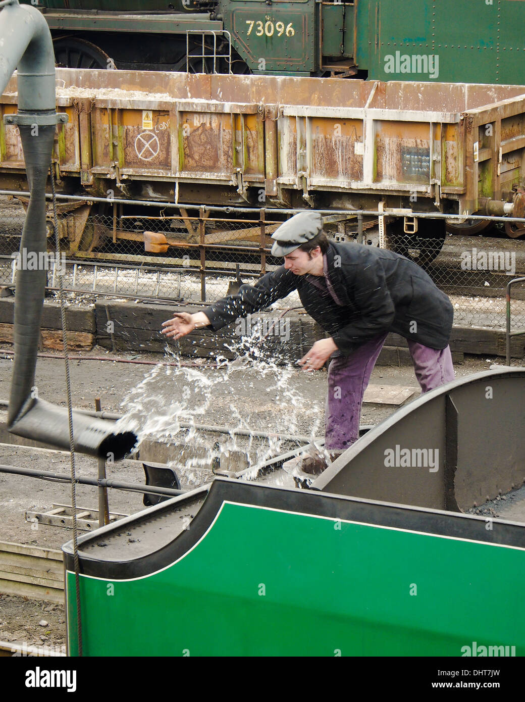 An engineer releases the water hose from a steam train having filled the tank with water. Stock Photo