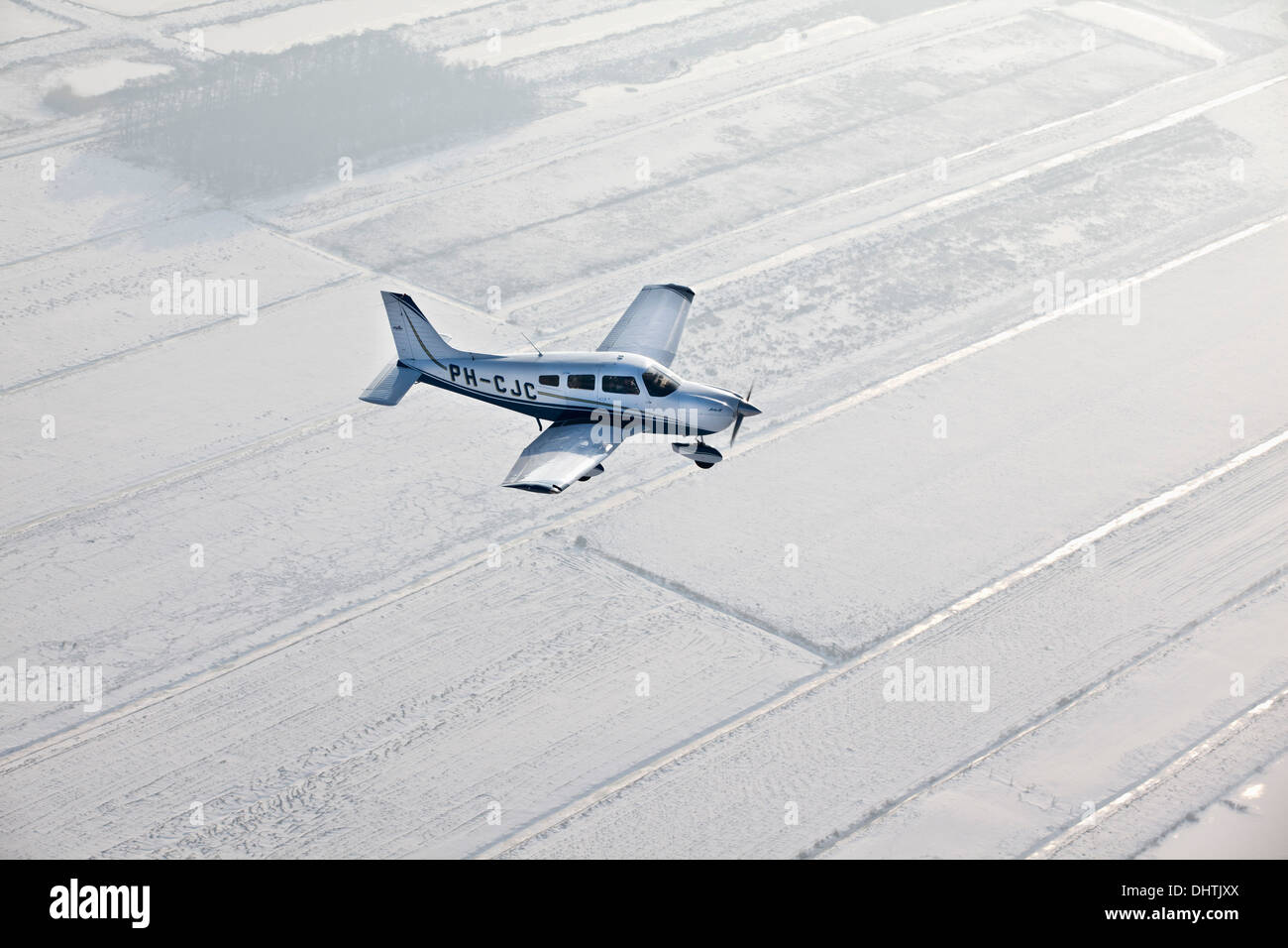 Netherlands, Loosdrecht, Small aircraft flying over snowy fields. Aerial Stock Photo