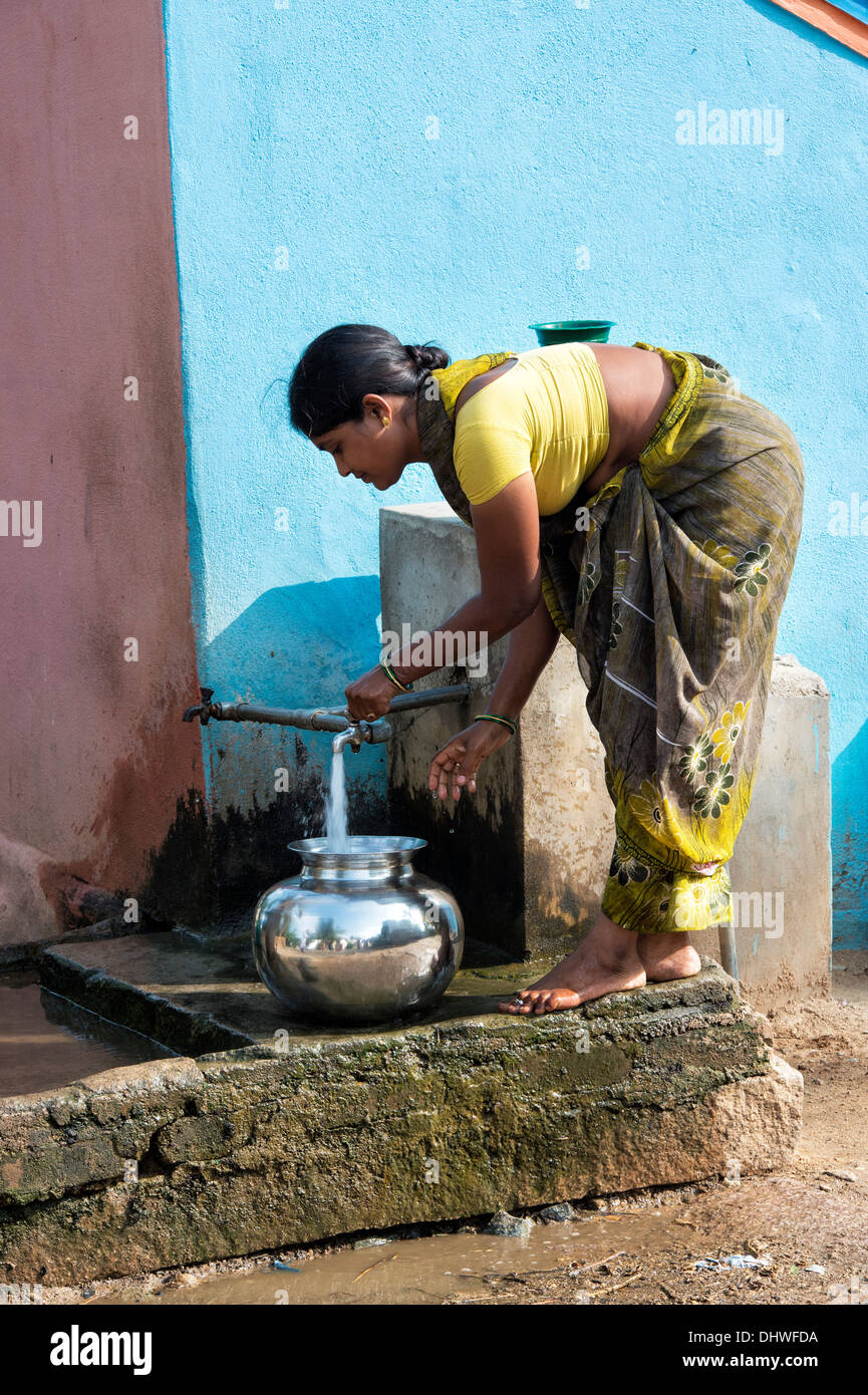 Indian woman filling a metal pot with water from a standpipe in a rural Indian village street. Andhra Pradesh, India Stock Photo