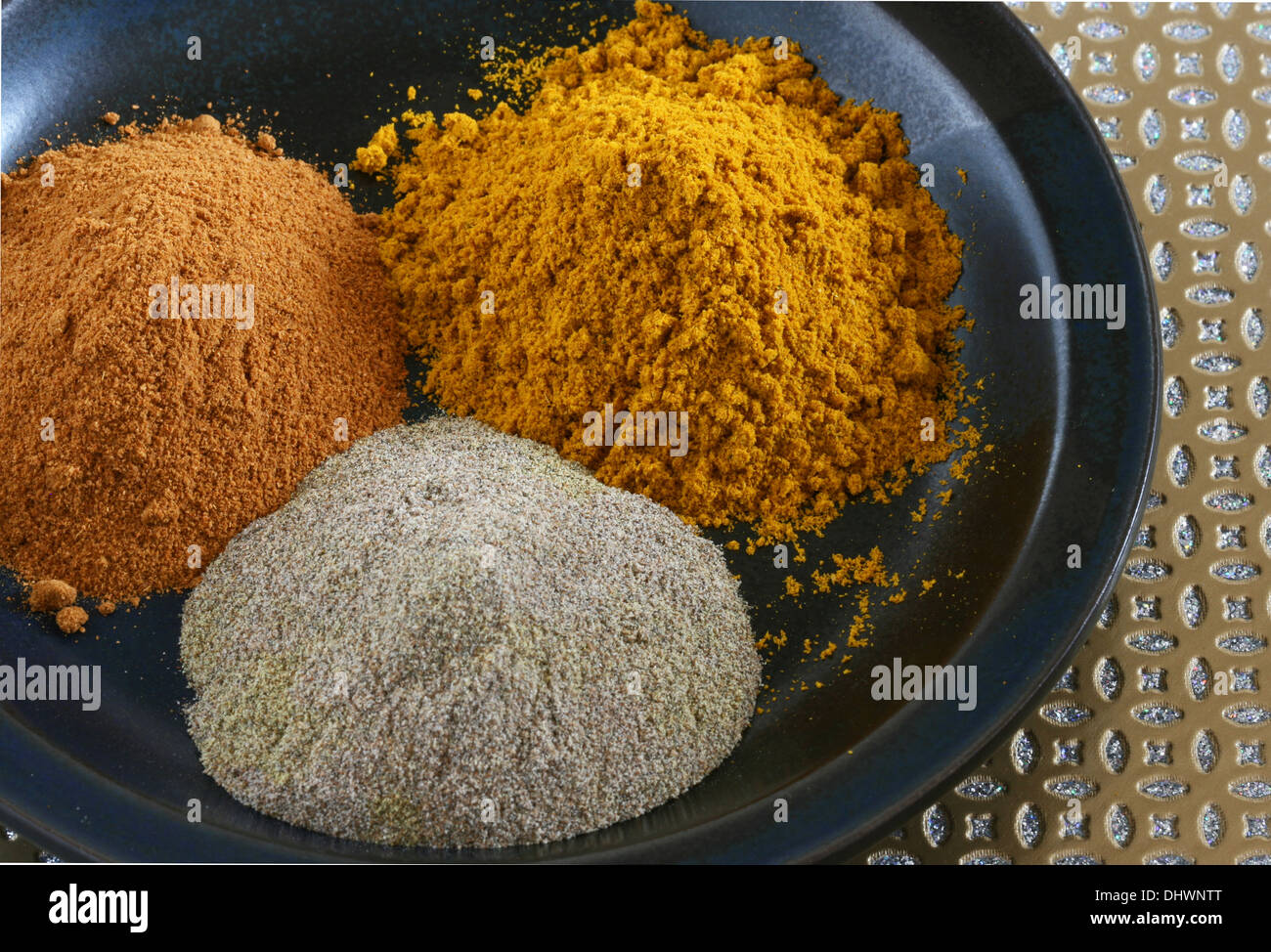 Three ground Indian spices on a plate; curry, cardamom, turmeric Stock
