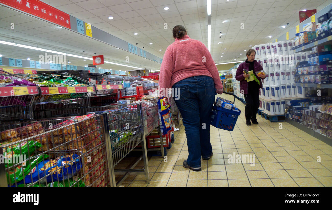 Rear view of an overweight  woman obesity shopping in an aisle of crisps (potato chips)  in an Aldi store UK Great Britain    KATHY DEWITT Stock Photo