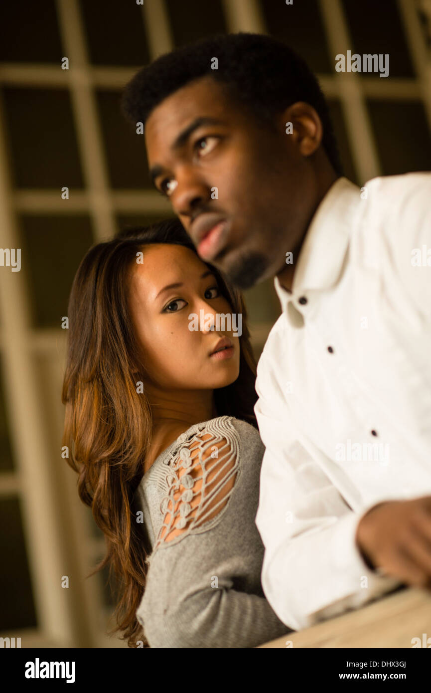 A young couple - asiatic chinese woman afro-caribbean black man - indoors, inside UK Stock Photo