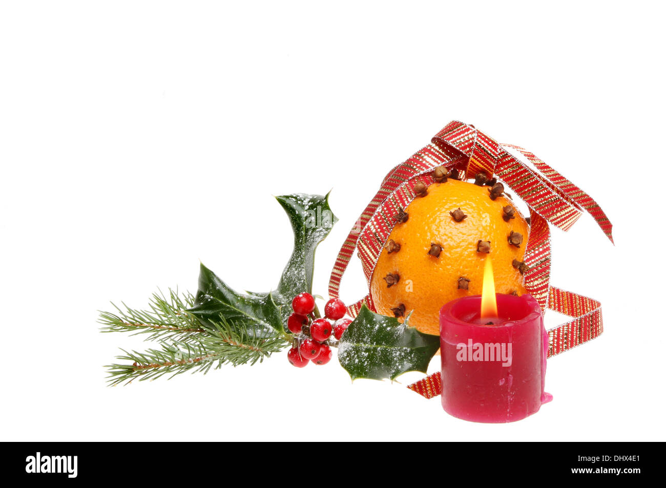 Christmas decoration of clove decorated orange, holly and pine needles and a burning red candle isolated against white Stock Photo