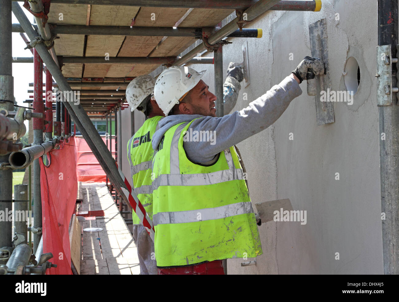 Two workmen apply concrete render to the exterior of public housing as part of refurbishment work including thermal overcladding Stock Photo