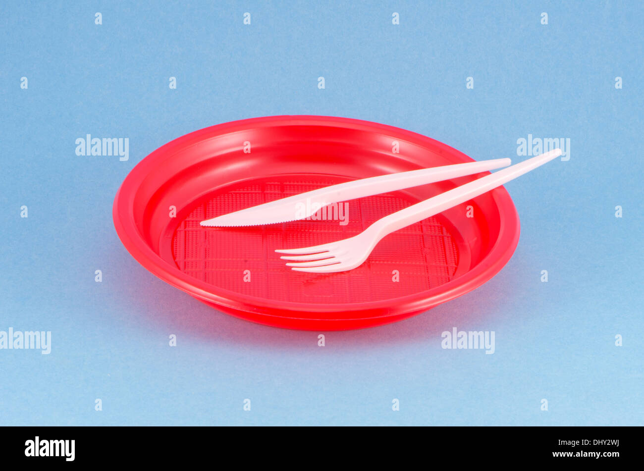 disposable plastic red plate on blue background with white fork and knife Stock Photo
