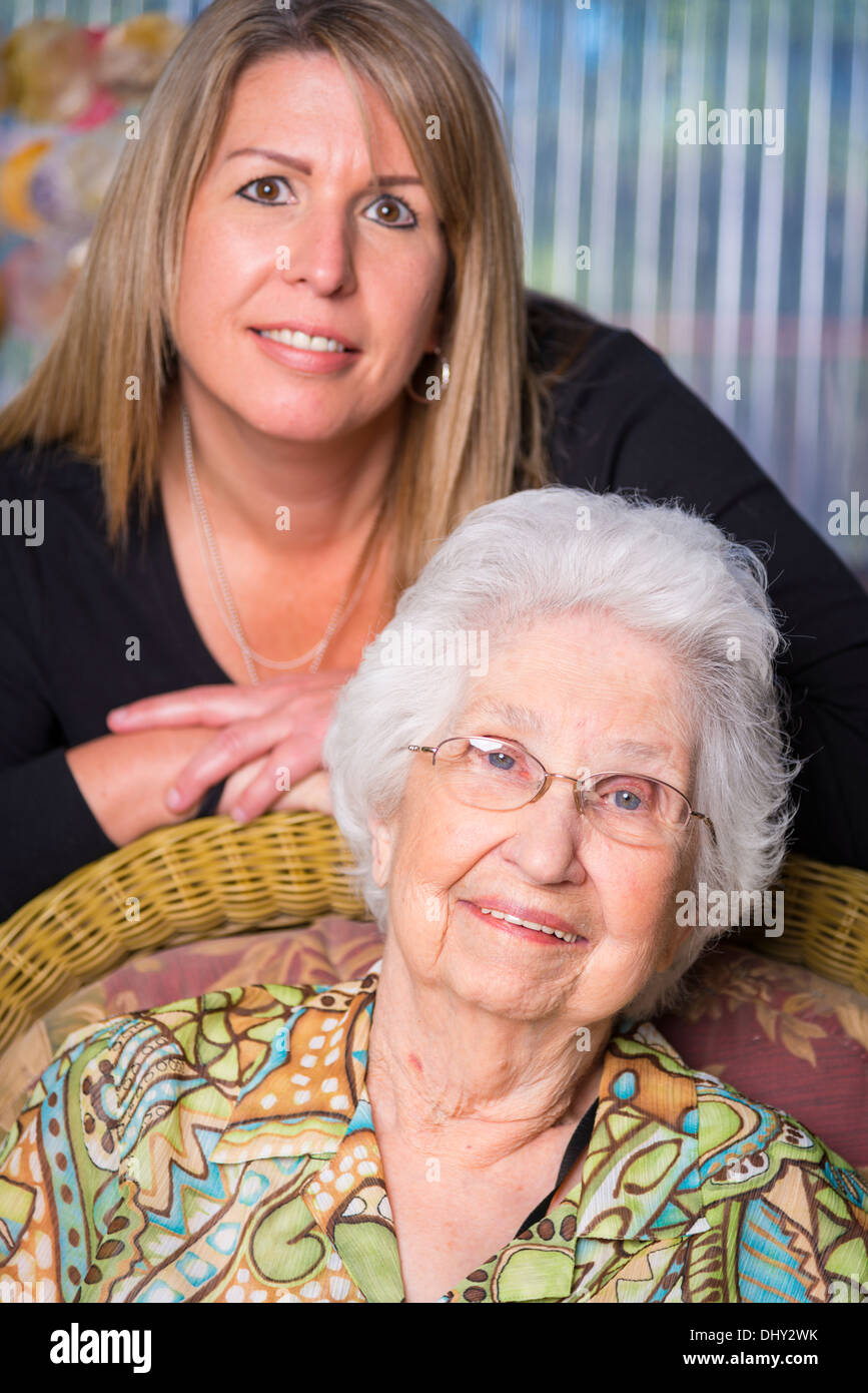 Portrait of elderly woman in her 90s with her mature granddaughter in the 40s. Both smiling while looking at camera. Stock Photo