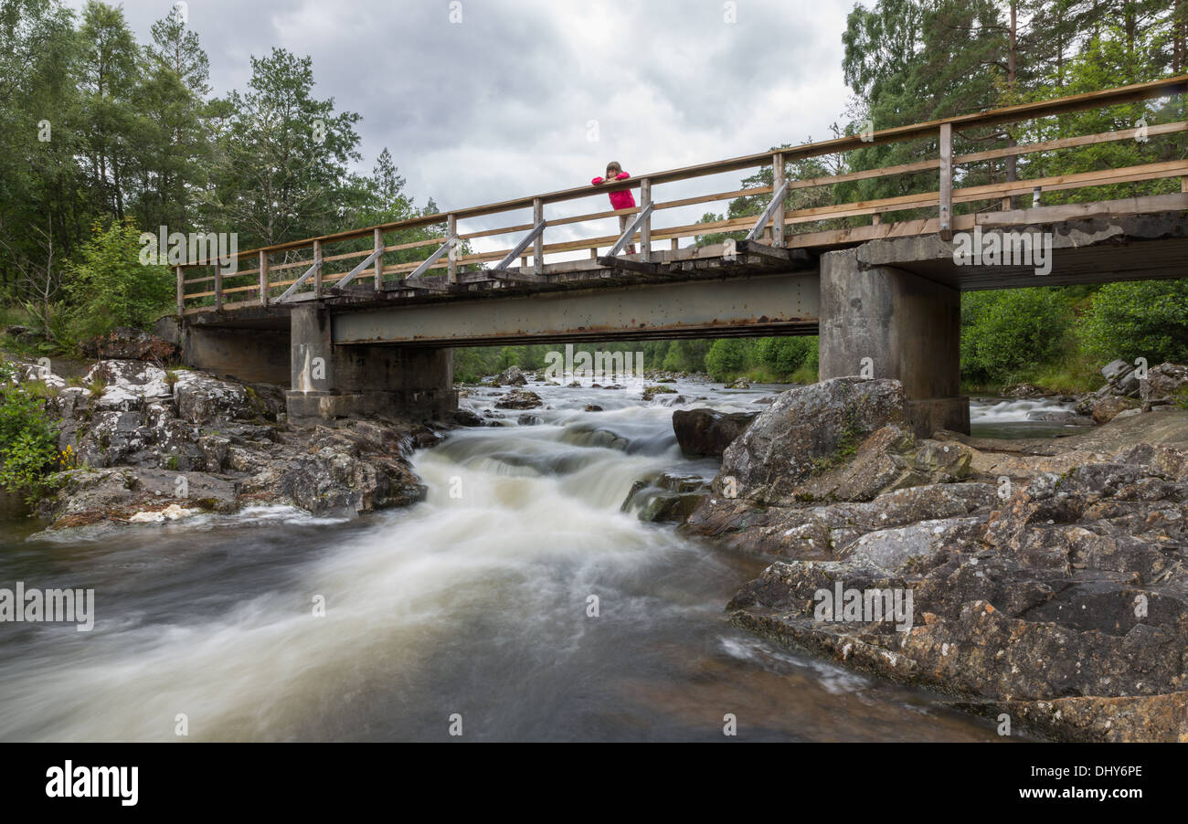 Young girl watches water flowing under a bridge in the Scottish Highlands Stock Photo