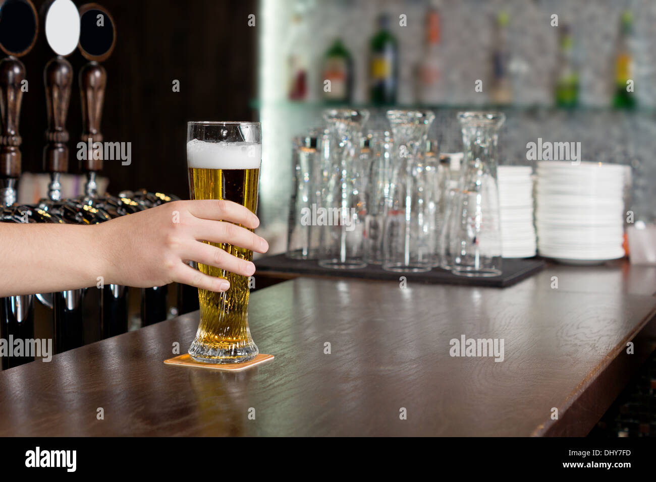 Hand of a man reaching for a pint of beer in a pub which is standing on a wooden bar counter Stock Photo