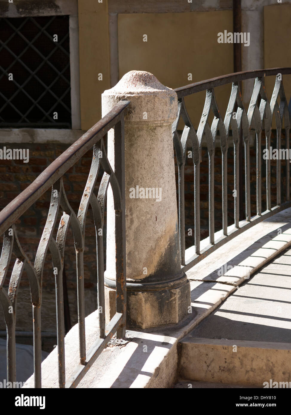 Sunlit, ornate, curved iron hand railings and stone pillar on arched bridge parapet, Venice, Italy. Stock Photo