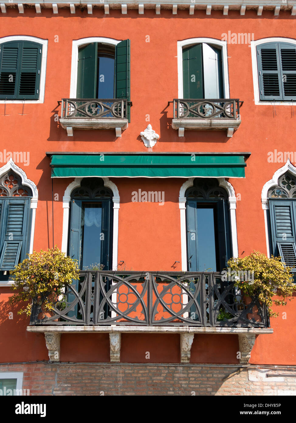 Terracotta orange red rendered Venetian house facade with ornate balconies and green window shutters, Venice, Italy. Stock Photo