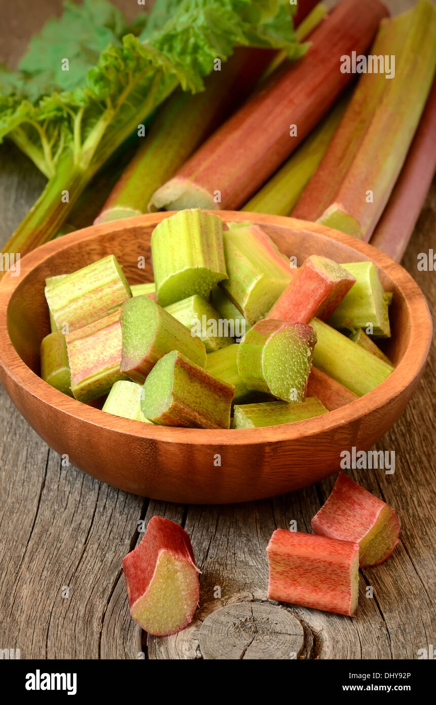 Fresh rhubarb in brown bowl on wooden garden table Stock Photo