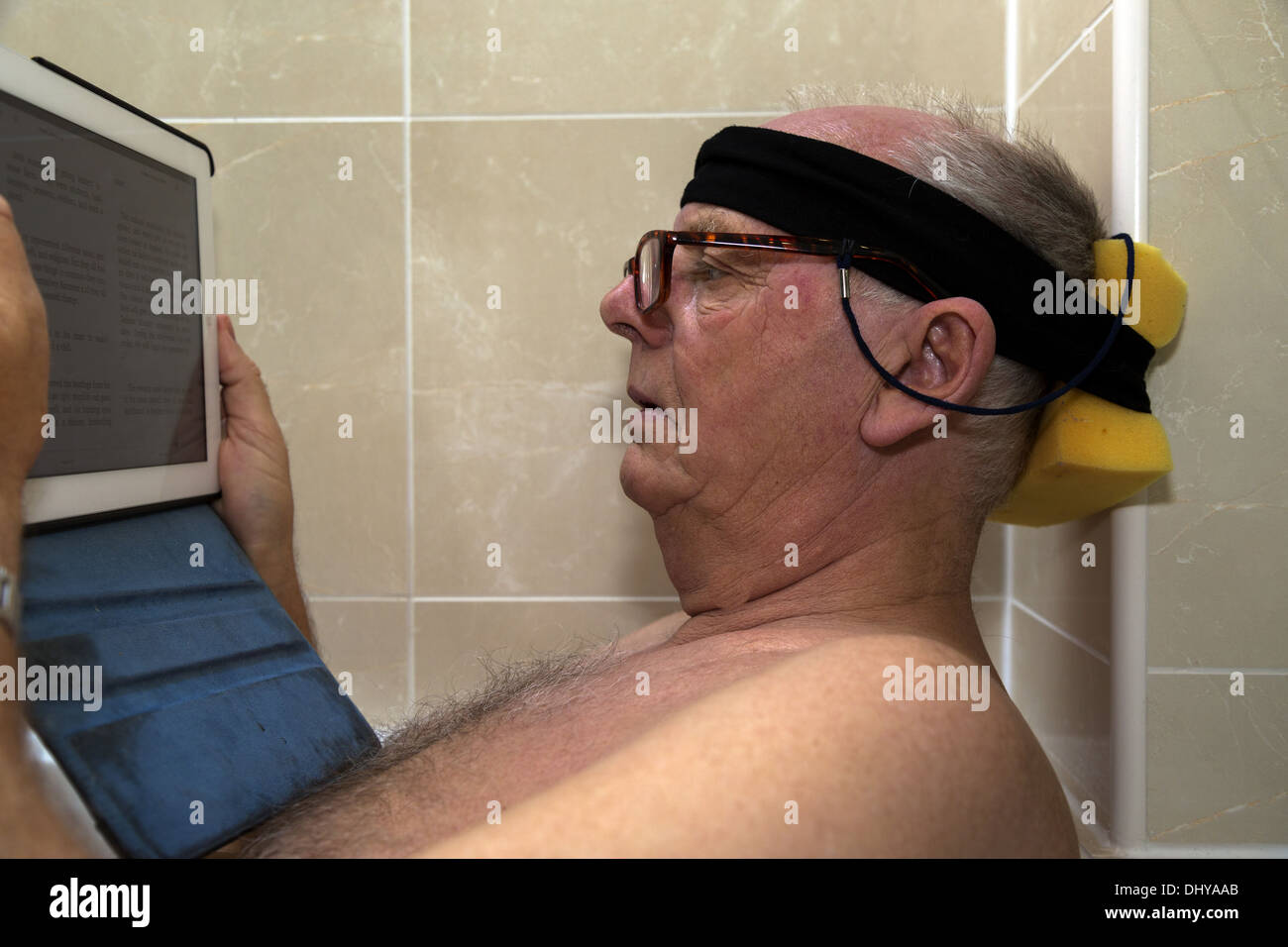 Senior man reading iPad in the bath resting his head on a makeshift headrest Stock Photo