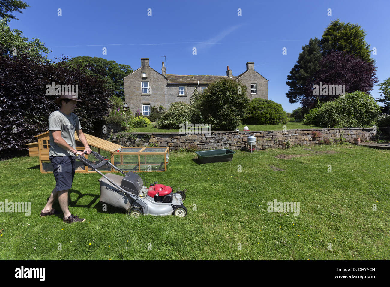 Man mowing the lawn in front of a large stone house Stock Photo