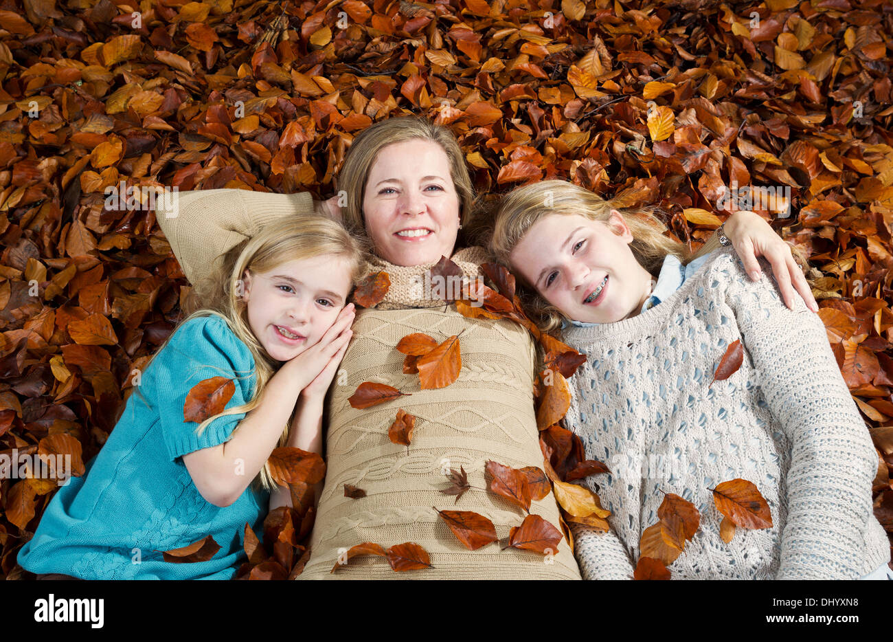 Horizontal photo of a happy mother with her daughters lying on a bed of autumn leaves Stock Photo