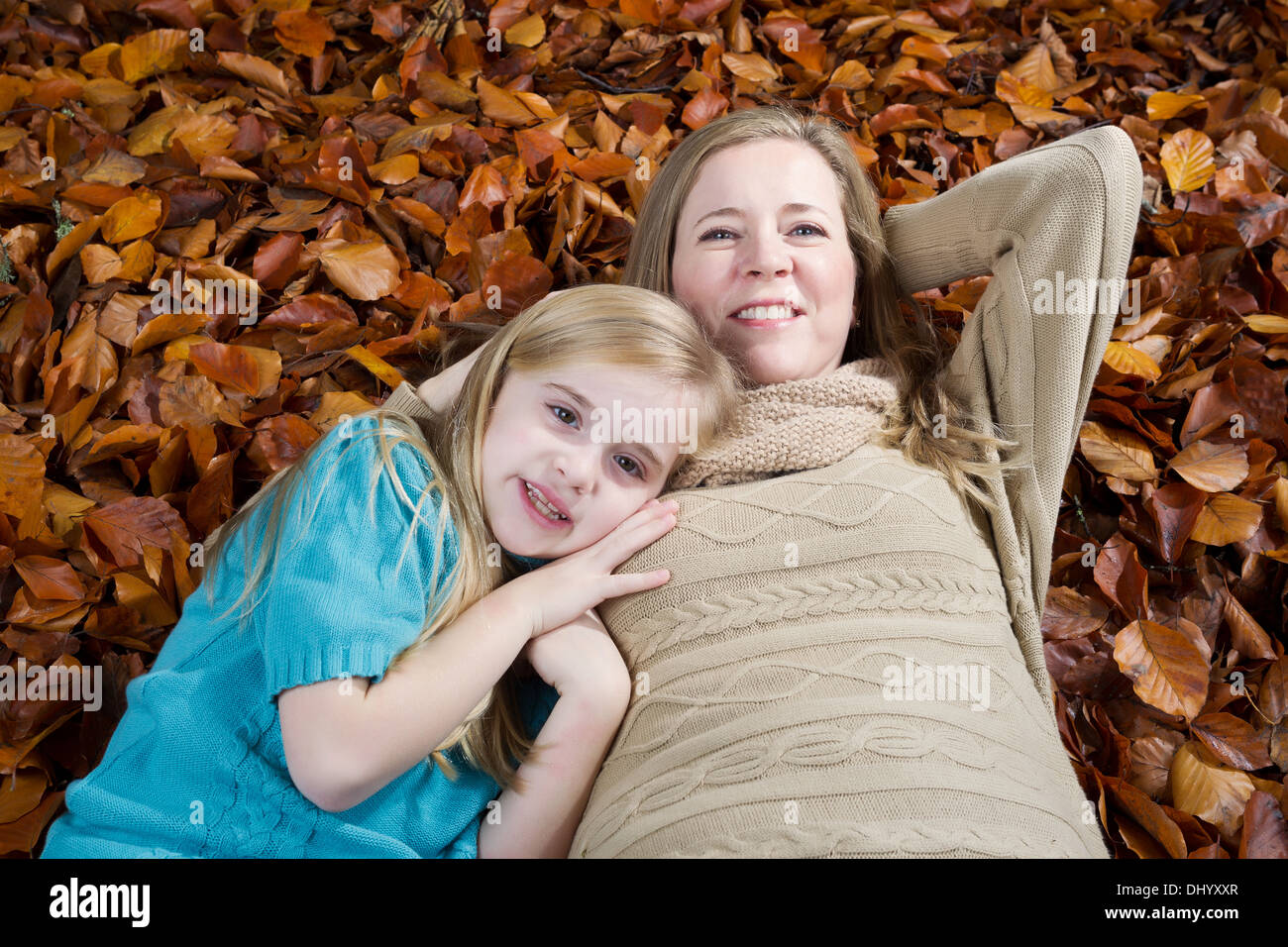 Horizontal photo of a happy mother with her young daughter resting on a bed of autumn leaves Stock Photo