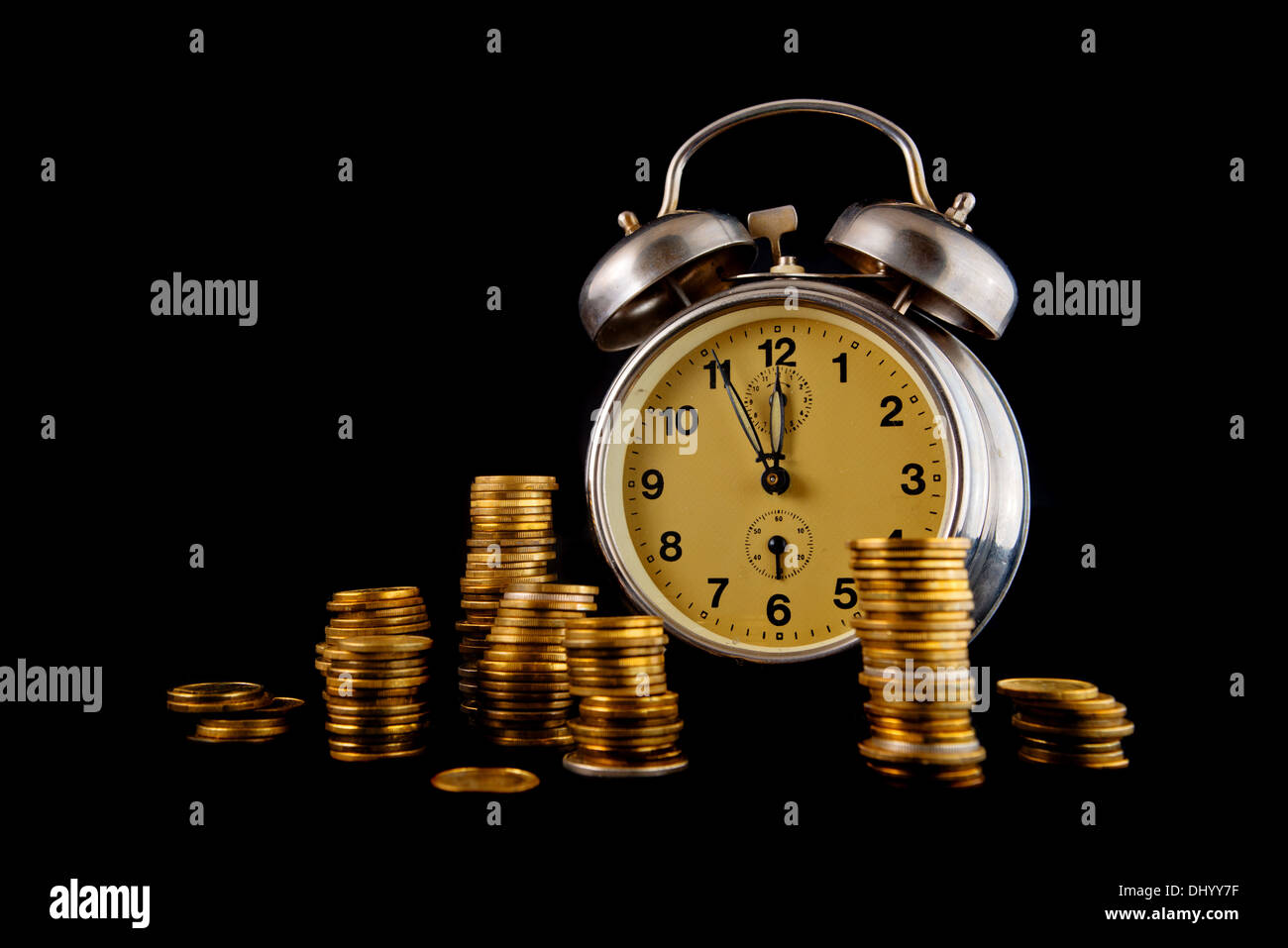 Golden coin stack and vintage clock on dark background. Time is money concept. Stock Photo
