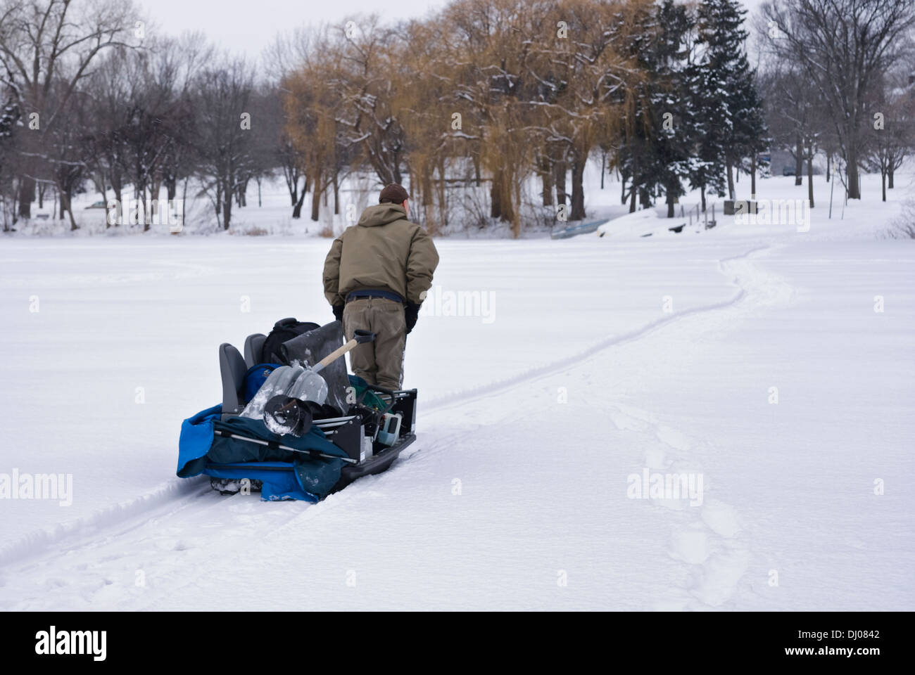 Man hauls his ice fishing shack on a sled across a frozen lake