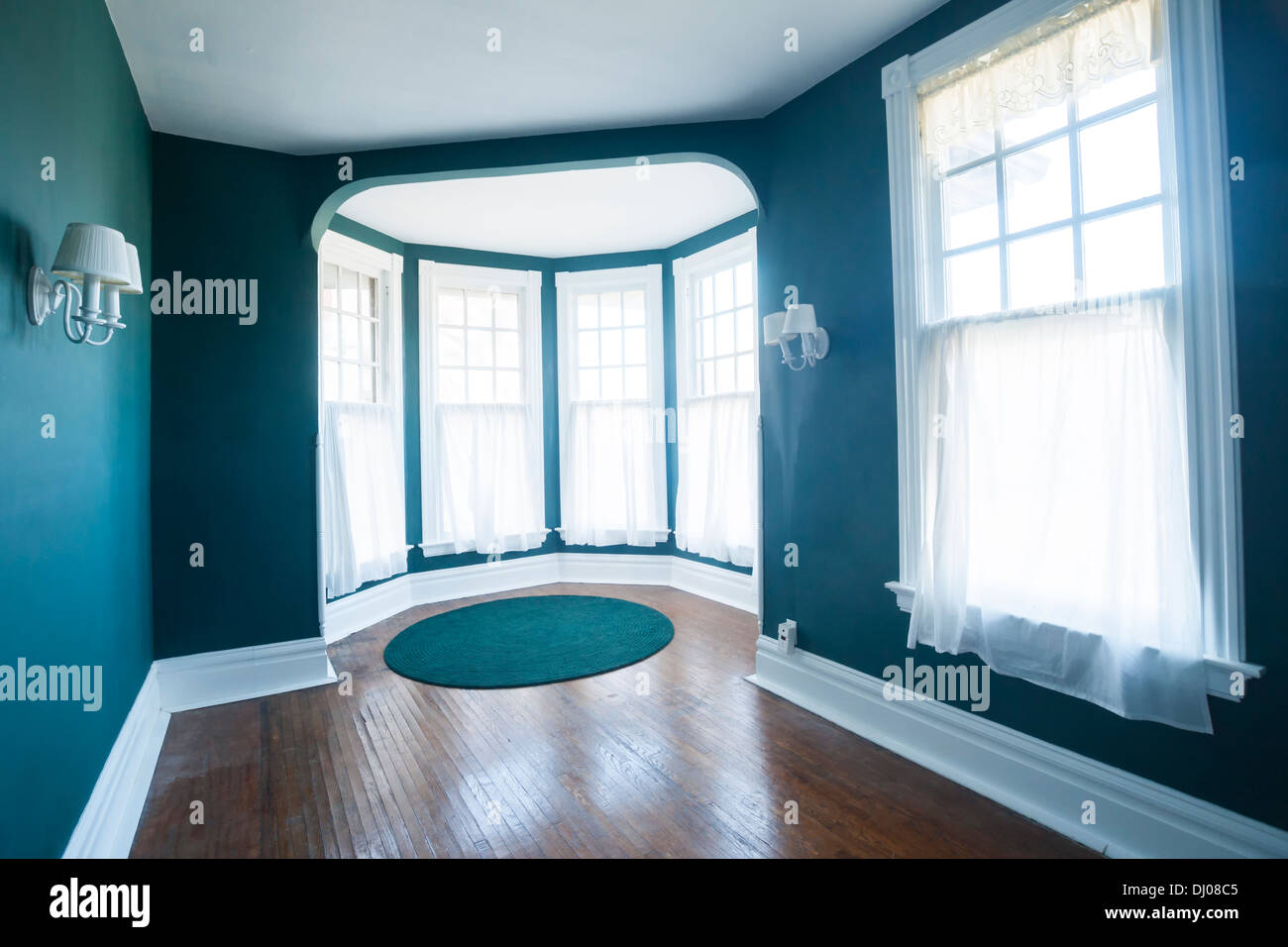 Empty room with 5 windows, sconces, and wood flooring inside a Tudor home, USA Stock Photo