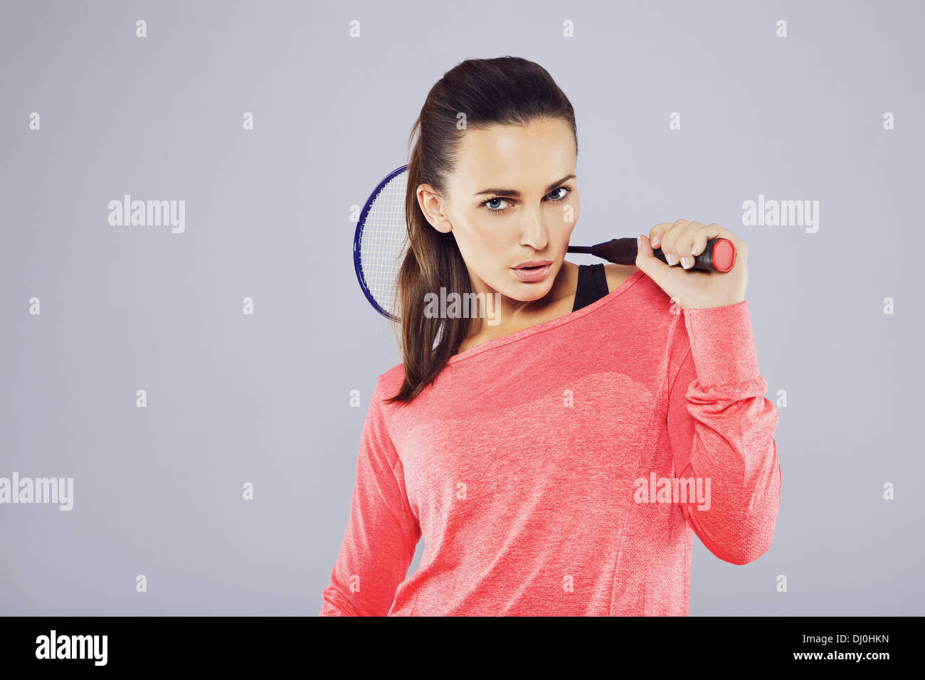 Portrait of pretty young girl holding a badminton racket looking at camera against grey background. Stock Photo