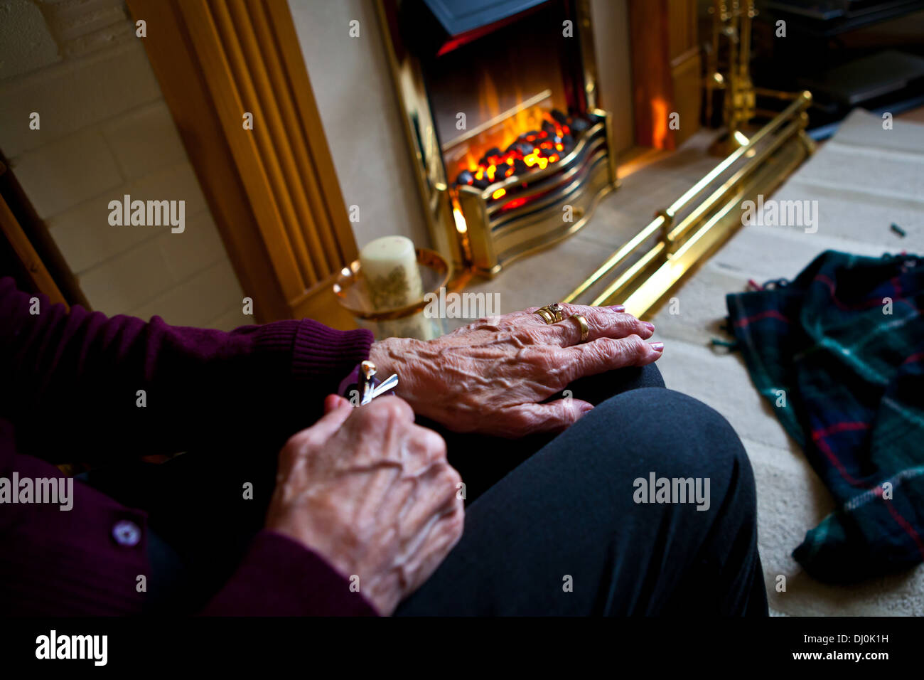 Elderly woman sitting near electric fire Stock Photo