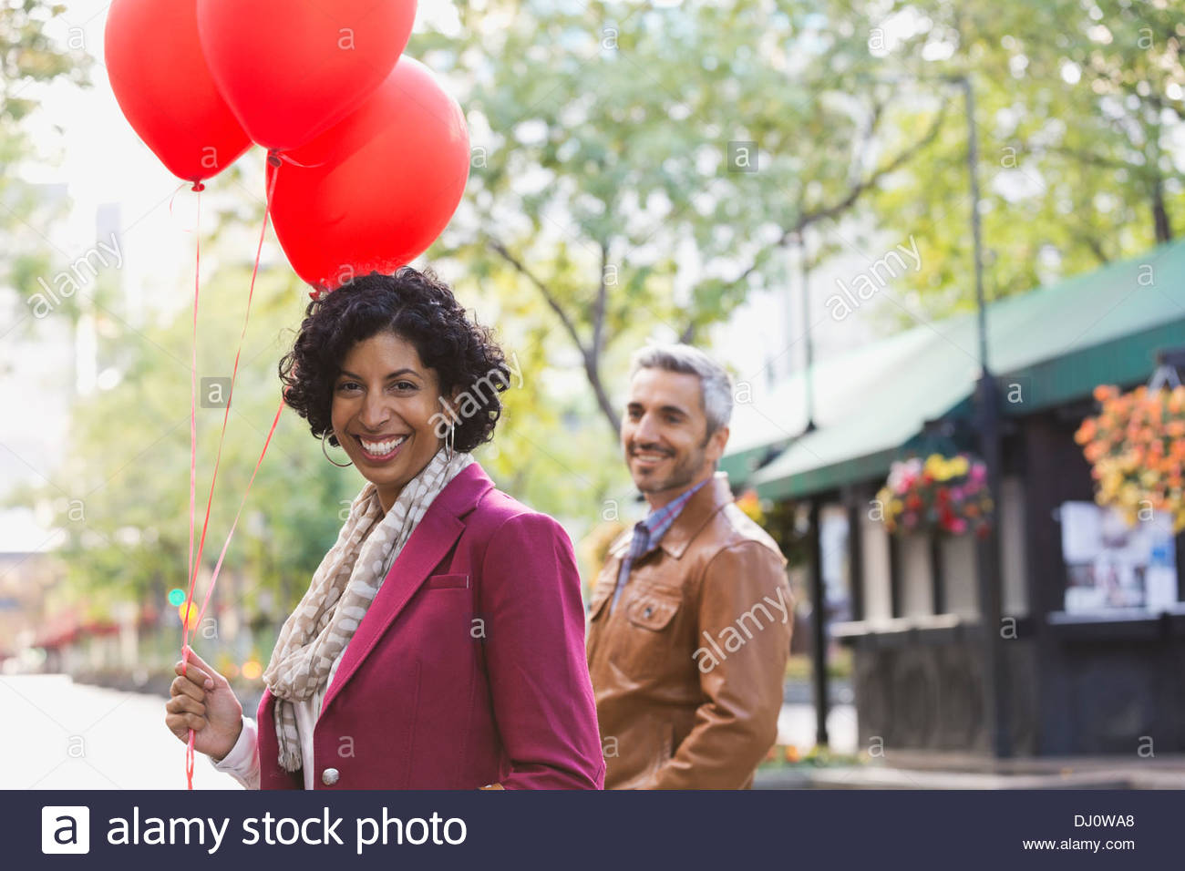 Portrait of happy woman holding red balloons outdoors Stock Photo