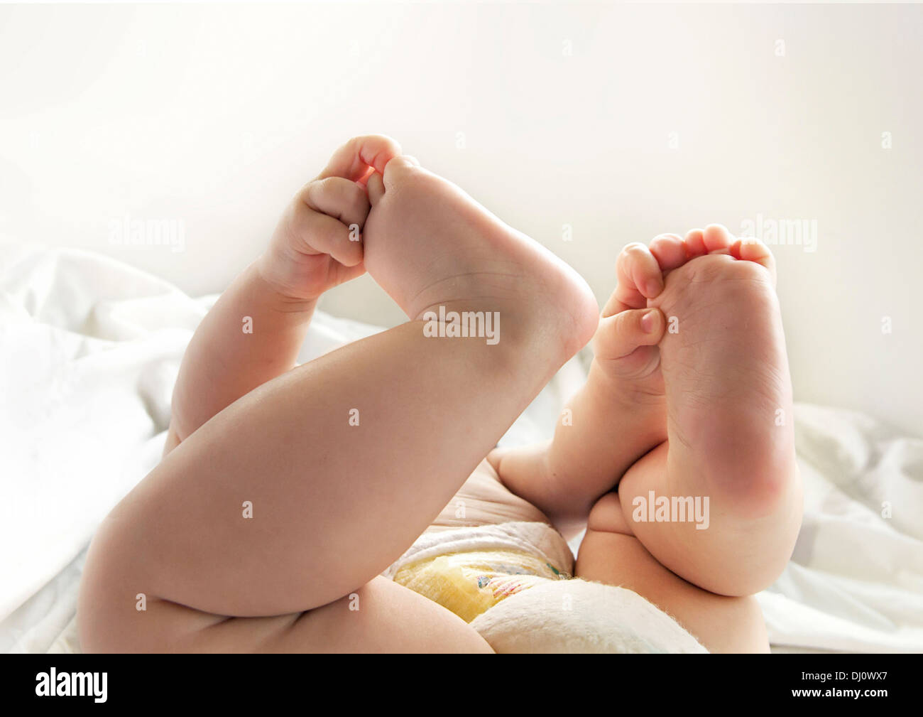 Baby's hands holding feet up in the air Stock Photo