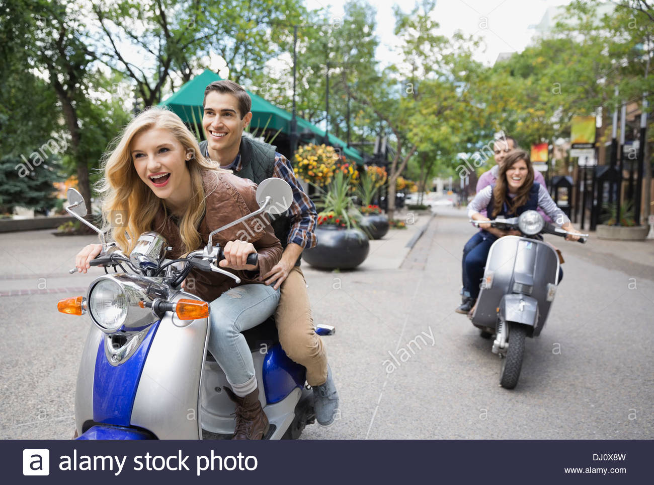 Two couples riding scooters on city street Stock Photo