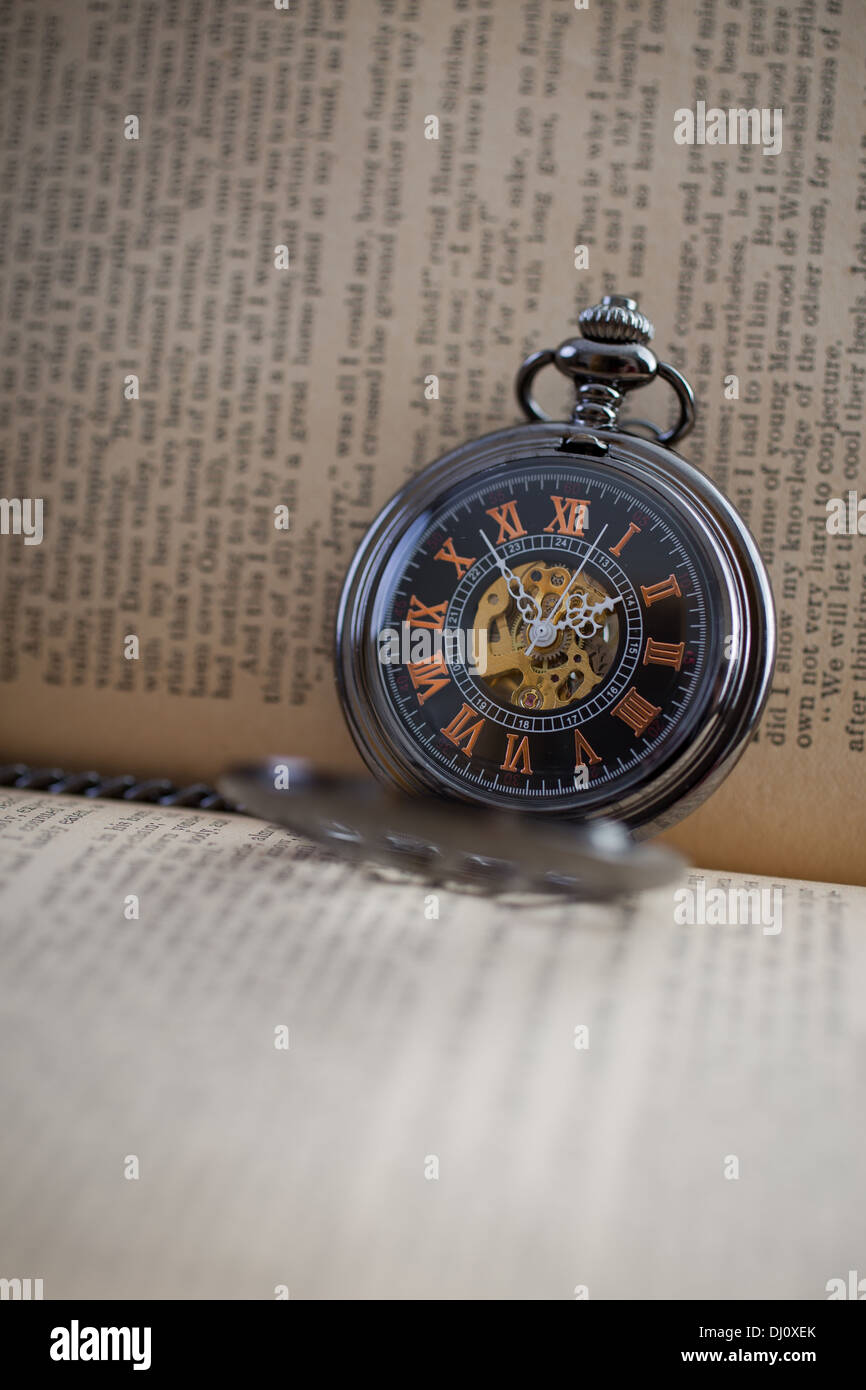 A pocket watch timepiece among the pages of a book. Stock Photo