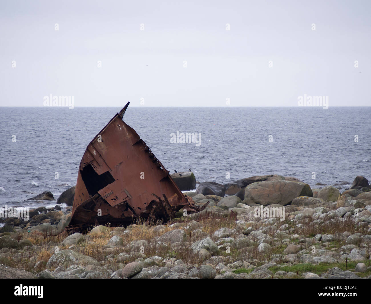 Rusty shipwreck on the shoreline of the North sea, Jæren near Stavanger Norway, rolling stones, stone wall and rough seas Stock Photo