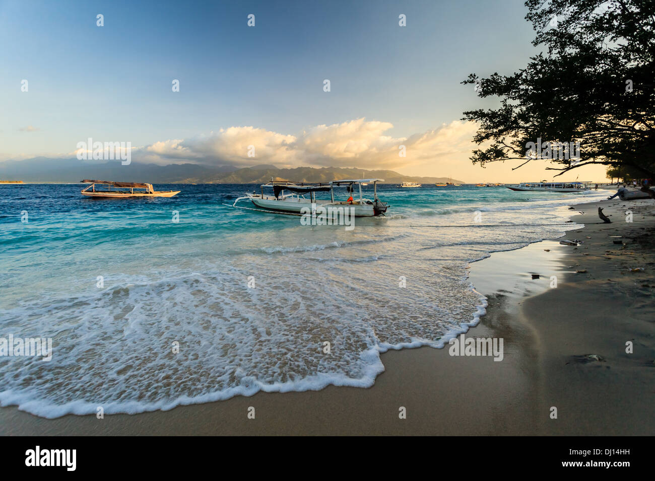 View across turquoise water to Lombok Island from Gili Trawangan beach at sunset with boats moored on the coast Stock Photo