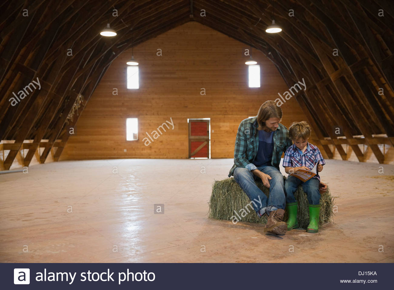 Portrait of father and son reading book on hay bale in barn Stock Photo