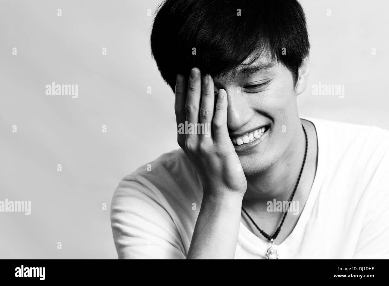Portrait of young man covering his face and smiling, black and white ...