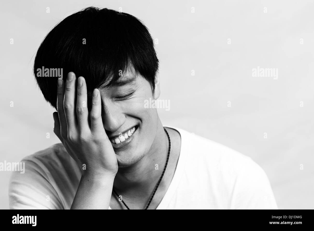 Portrait of young man covering his face and smiling, black and white ...