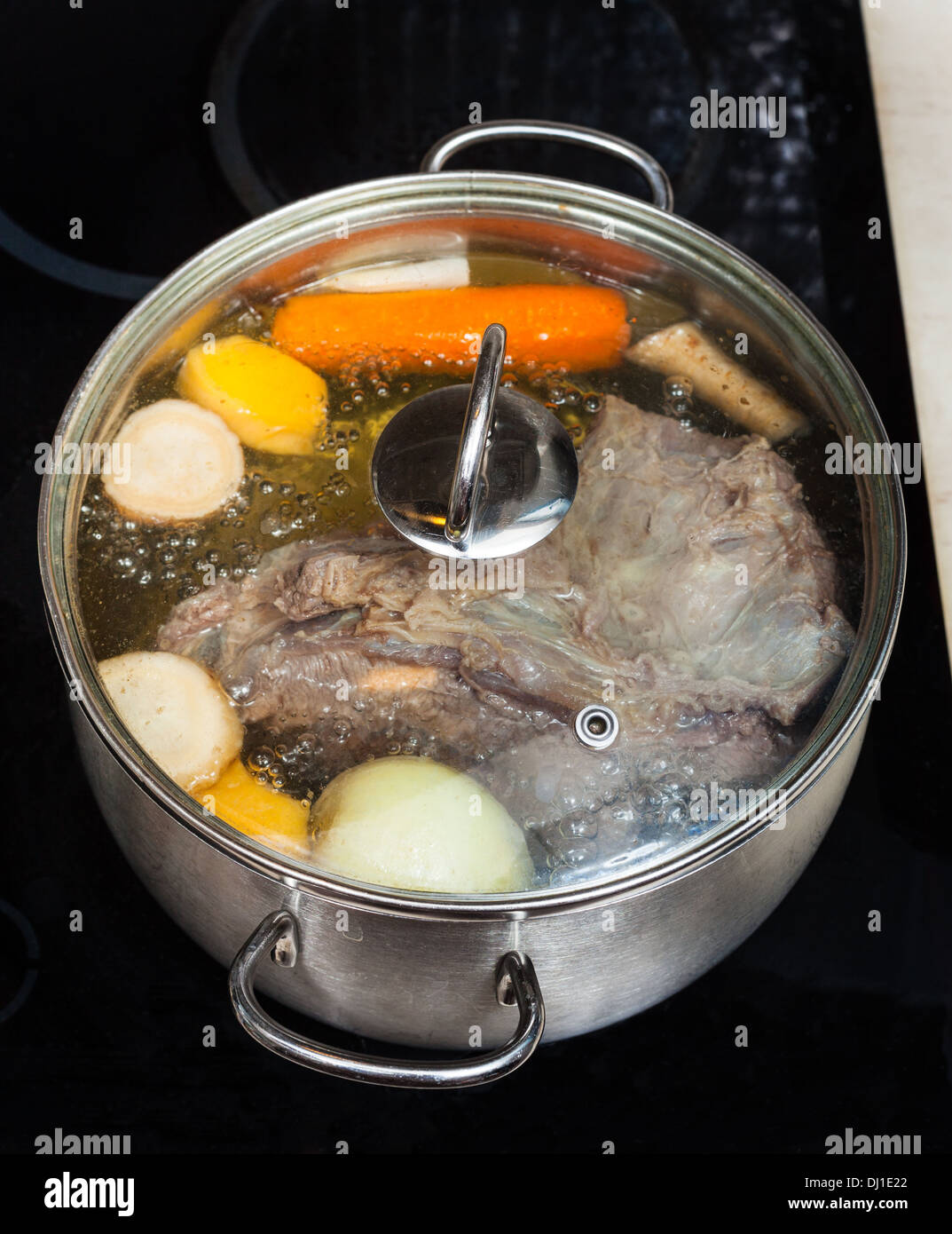 boiling of beef broth with seasoning vegetables in pan on glass ceramic cooker Stock Photo