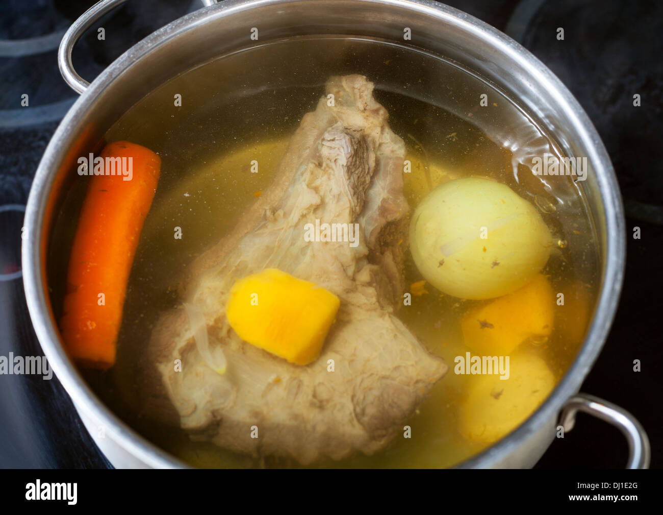 beef broth with seasoning vegetables in open pan on glass ceramic cooker Stock Photo