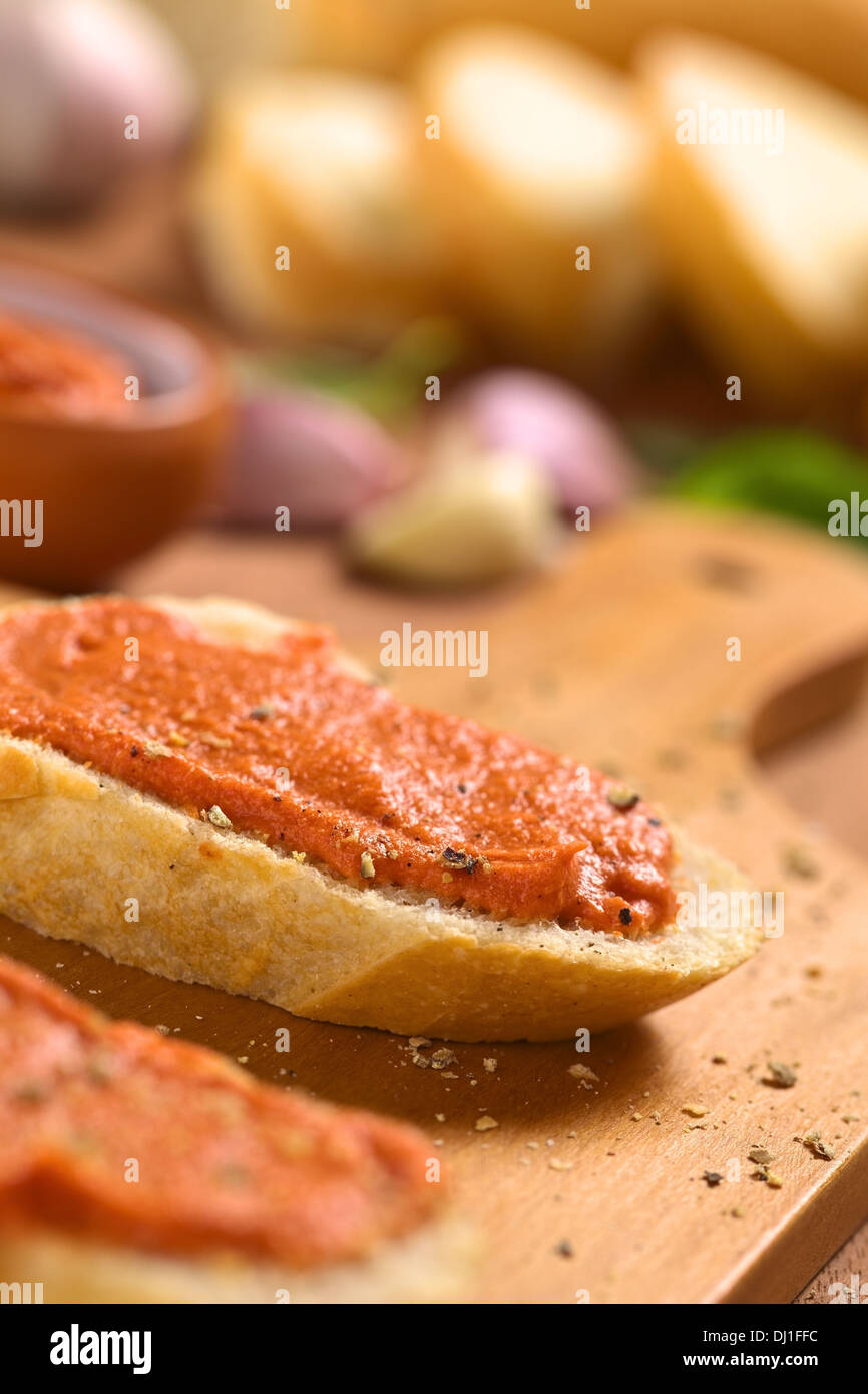 Homemade tomato-butter spread on baguette slices with fresh ground pepper on wooden board Stock Photo