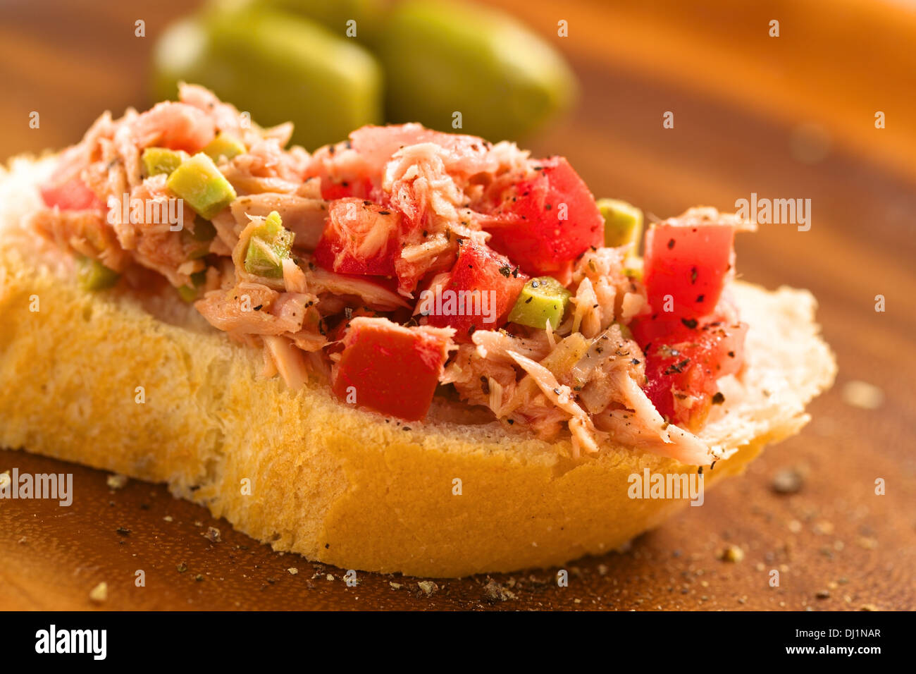 Slice of baguette with fresh tuna, green olive and tomato spread