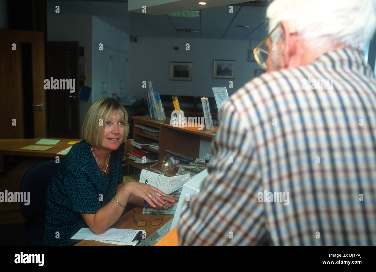 GP receptionist talking to elderly male patient, Belmont Medical Centre