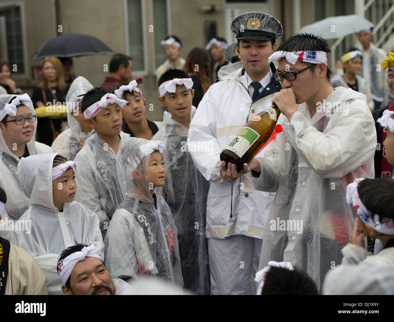 Reveler Drinking Sake while children and police watch, Karatsu Kunchi Festival, Karatsu City, Saga Prefecture, Japan Stock Photo