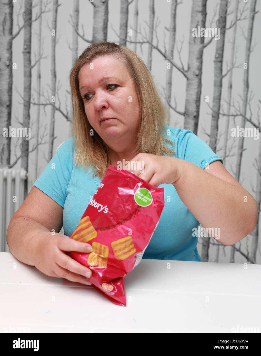 Overweight woman eating a bag of family-sized crisps. Stock Photo