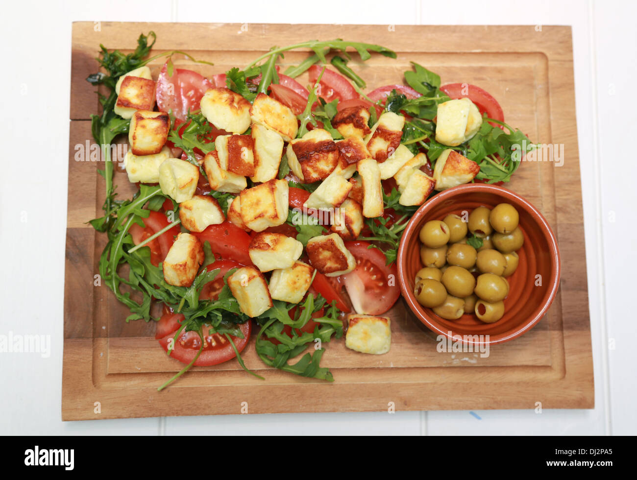 Halloumi salad and green olives on a wooden board. Stock Photo