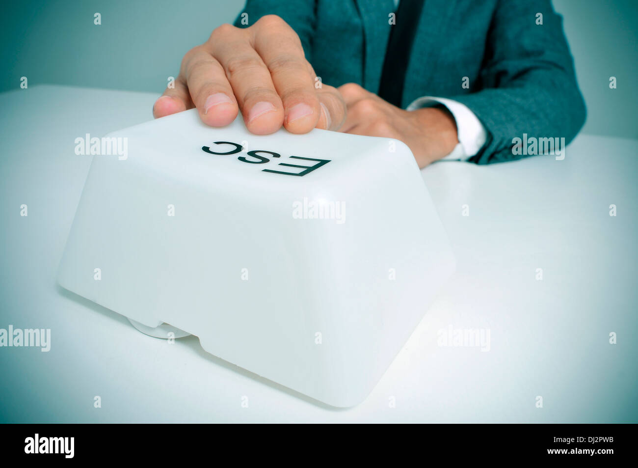 man wearing a suit sitting in a table pressing a giant escape key with his hand Stock Photo