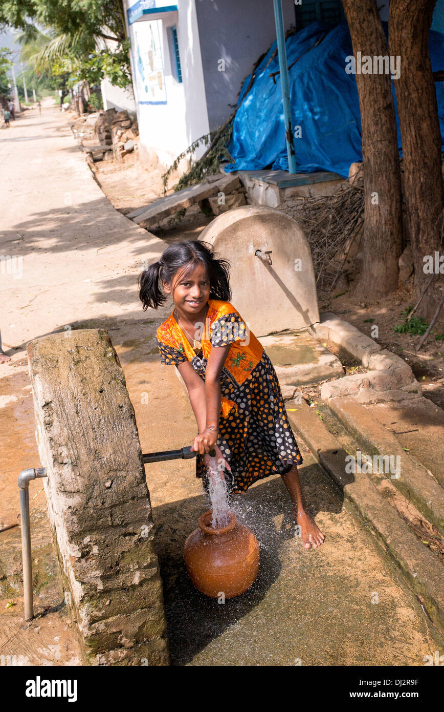 Indian girl filling a plastic pot with water from a standpipe in a rural Indian village. Andhra Pradesh, India Stock Photo