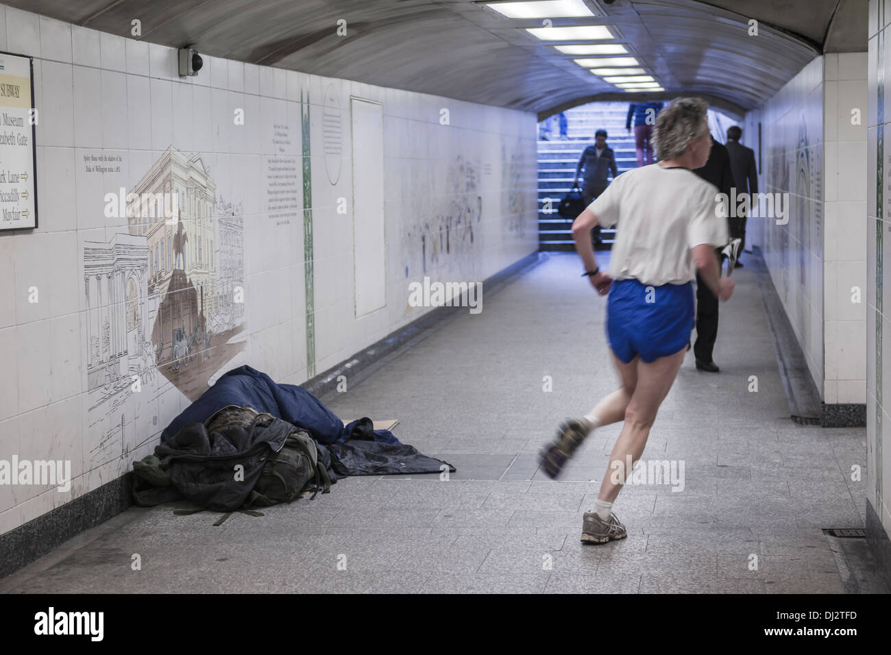 A jogger passes a man sleeping rough in a central London subway. Stock Photo