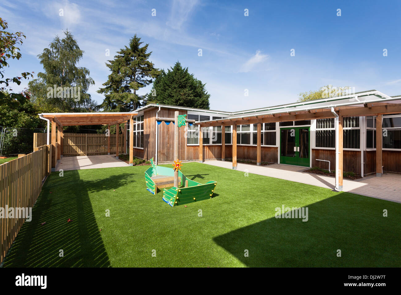 Infant school fenced grassed playground by timber clad classrooms. Stock Photo
